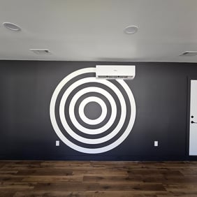 Black accent wall with a bold bullseye design painted in the center, featuring a sleek floating shelf for a modern game room 