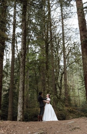 a bride and groom standing in a forest