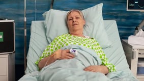 Elderly woman lying in hospital bed with vital signs monitor and IV line