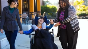 Happy disabled boy in wheelchair outdoors with two smiling female caregivers