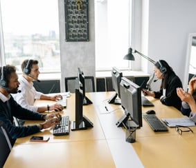 Smiling customer service representative wearing a headset, sitting at a desk with a computer