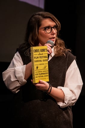 A woman speaks on a mic to present a book about film festivals