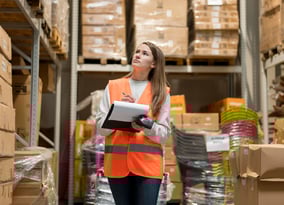 a woman in a safety vest holding a clipboard in a warehouse