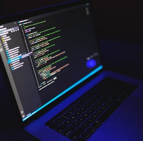 A laptop displaying colored code lines on a dark-themed text editor screen.