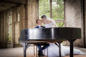 Brautpaar mit Hochzeitskleid und Anzug, während ein Pianist in einem alten Raum spielt.