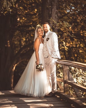 Brautpaar in eleganter Hochzeitskleidung auf einer Holzbrücke umgeben von Bäumen