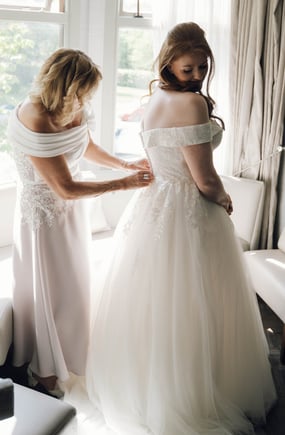 a woman in a white dress is helping a woman in a wedding dress
