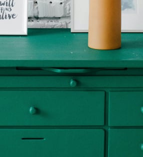 a green dresser with a vase of dried grass in front of a brick wall