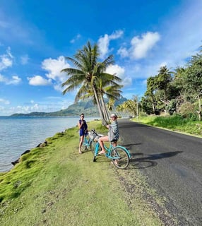 Eva and Manon cycling on a palm-lined road in Bora Bora, French Polynesia.
