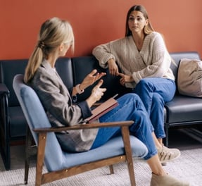 a woman sitting on a couch talking to another woman