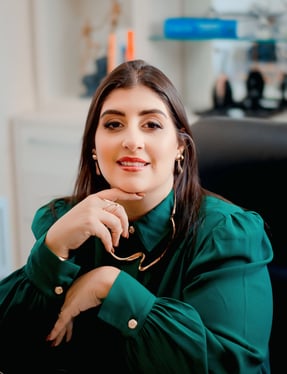 Foto da psicóloga sentada na cadeira do consultório, vestindo uma blusa verde escura e sorrindo
