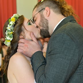 Hochzeitspaar küsst sich, umgeben von applaudierenden Gästen.
