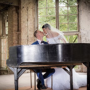 Brautpaar mit Hochzeitskleid und Anzug, während ein Pianist in einem alten Raum spielt.