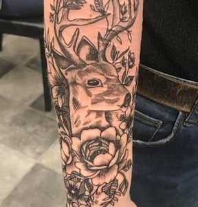 a tattoo of flowers and a buck cover self harm scarring on the arm of a white person