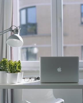 Modern home office desk with a laptop, desk lamp, green plants, and eyeglasses
