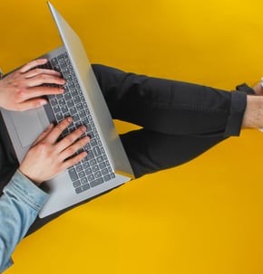 a man sitting on a yellow floor with a laptop propped on his legs