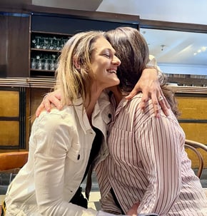 Coach Caroline, hugging a female client in a cafe.