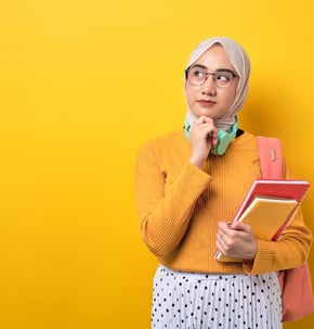 a muslim girl looks thoughtfully off to the side. she's standing on a yellow background.