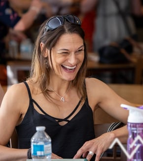 Lady laughing sitting at a table she has sunglasses on her head