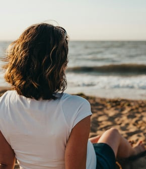 Femme assise seule sur la plage, face à la mer, et regarde un petit garçon jouer au bord de l'eau