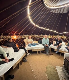 Photo of mens group with six men taking place in a yurt with wood stove