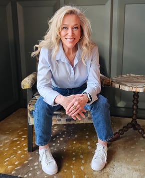 a blond woman sitting in a chair. she's wearing a blue button down shirt.