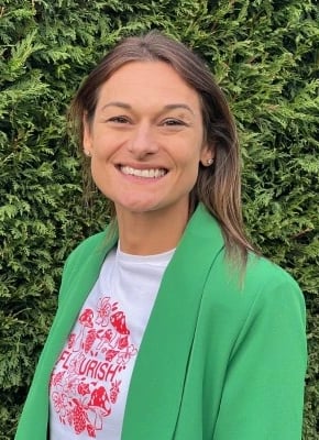 Lady stood before a hedge in a green coat smiling