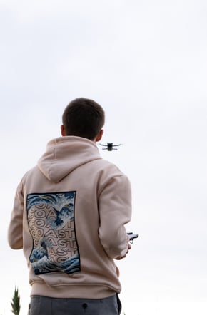 a man in a hoodie controlling a drone flying in front of him