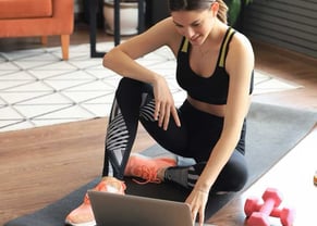 Mulher sorridente com roupa de ginástica fazendo exercícios em casa com tapete de yoga e halteres