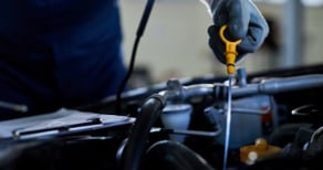 Close-up of an auto mechanic checking engine oil with a dipstick inside a vehicle repair shop.