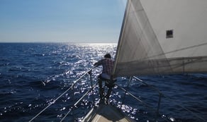 Un hombre sentado en la proa de un velero, con la vela a su espalda, navegando