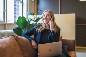 Mulher sorrindo enquanto fala ao telefone, com um laptop no colo.