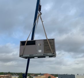a crane is lifting a ac unit to replace and install