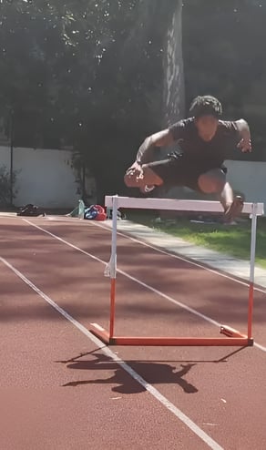 Jaison rakesh from pace sports is jumping over a hurdle on a track