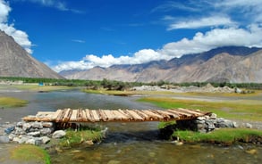 a wooden bridge over a river with a mountain in the background