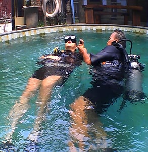a dive master and student in scuba gear in a pool geting the introduction dive course