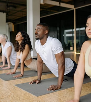 Grupo diverso de personas de varias edades practicando yoga o pilates juntos en una clase presencial, ilustrando las dinámica