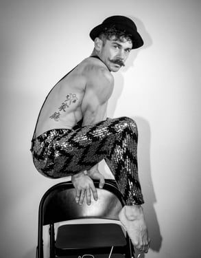 Black and white portrait of muscular circus performer suspended over chairs with shiny pants