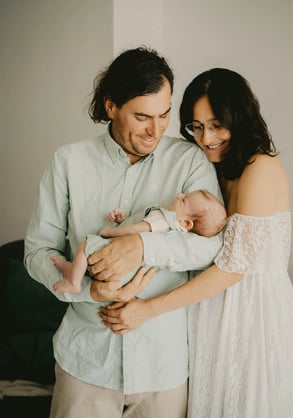 Parents souriants à la maison, regardant leur bébé dans les bras du papa – séance naissance domicile