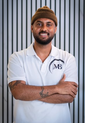 well lit Portrait photo of Maji, Co-owner of MB Barbers Manchester, posing with a smile and his arms crossed
