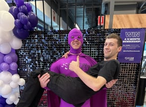 Mr. Anytime Fitness holding a staff member in his arms, posing for a picture in front of the black shimmer wall and balloon g
