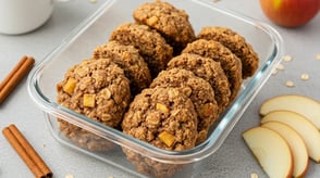 Glass container of apple oatmeal cookies with cinnamon sticks and apple slices.