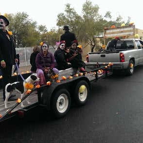 People with white facepaint sitting in trailer being pulled by truck at Halloween Parade