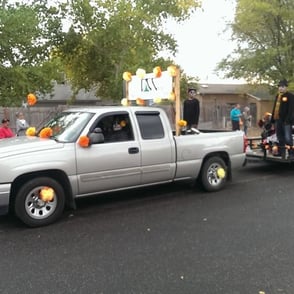 Truck at Halloween parade with large DCCNM sign pulling trailer covered in orange puff decorations.