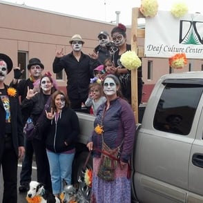 People with white face paint holding up ILY sign. Truck with DCCNM Logo in the background