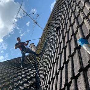 Artisan couvreur en intervention sur une toiture, effectuant un nettoyage haute pression à Belfort, équipé de harnais de sécu