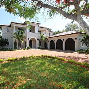 spanish style luxury home with an L shaped driveway and trees and red flowers and autumn leaves