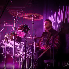  arthur debary le batteur jouant de la batterie lors du faster than light festival illuminé d'un spot rose, devant notre logo