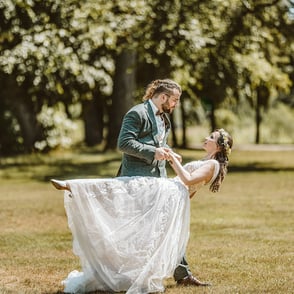 Ein Paar tanzt in einem grünen Park, das Brautkleid schimmert im Sonnenlicht.
