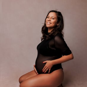 Femme enceinte assise à genoux et de profil avec un body noir pour une photo simple et glamour